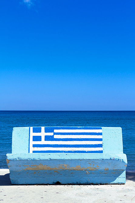 Blaue Bank mit griechischer Flagge am Meer - Blue bench with greek flag at the sea